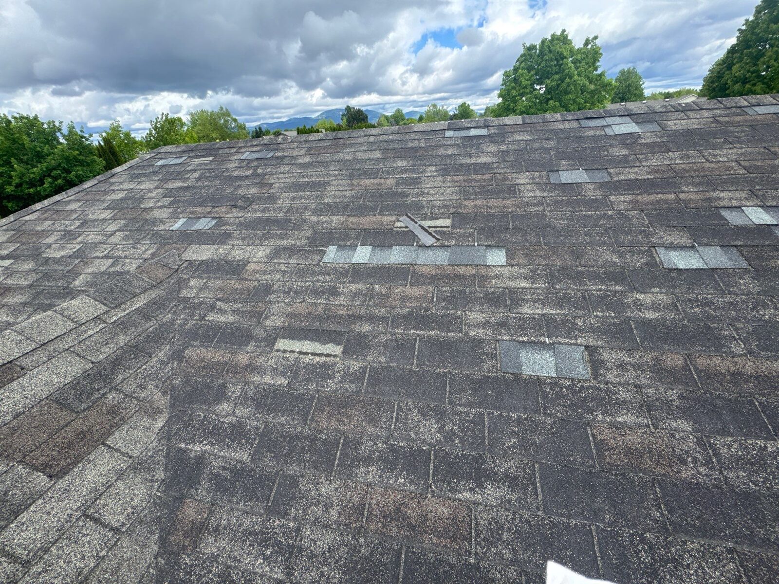 Wind-damaged residential roof in North Idaho with lifted shingles after a storm