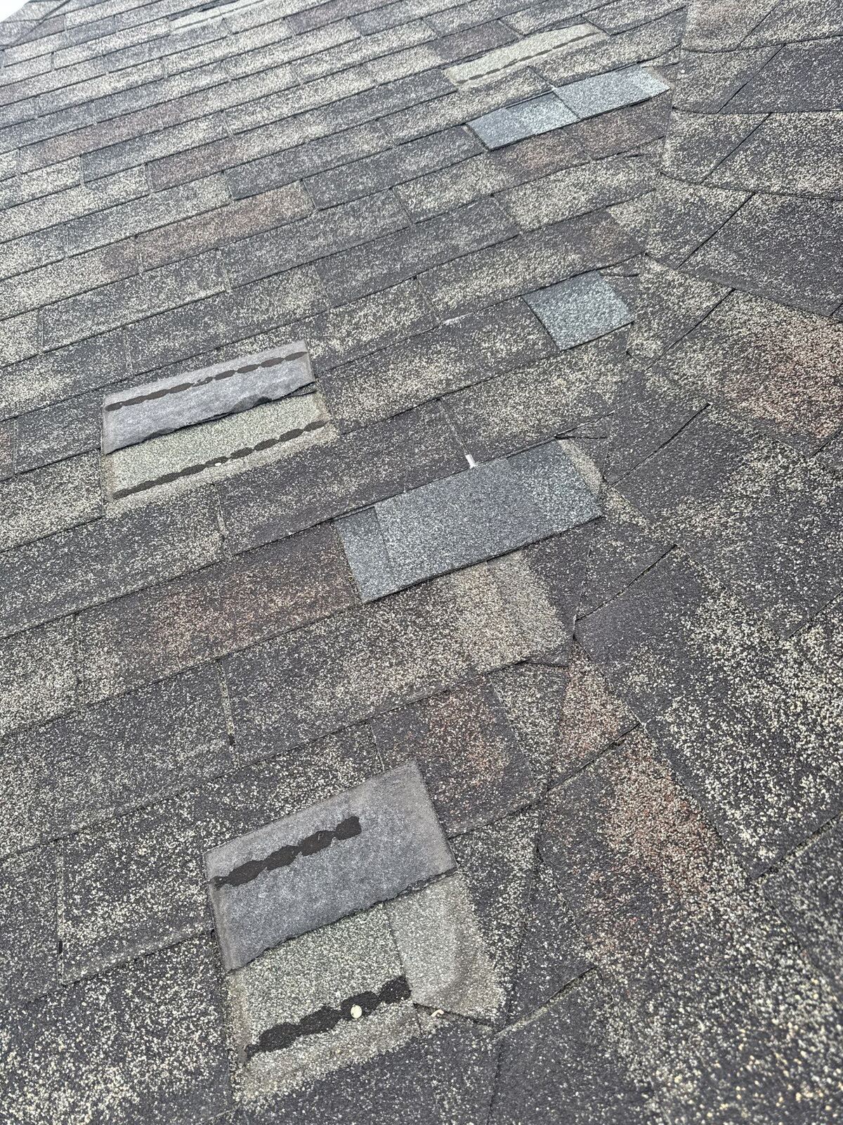 Wind-lifted and broken shingles on a North Idaho roof, the kind of damage that often qualifies for an insurance claim