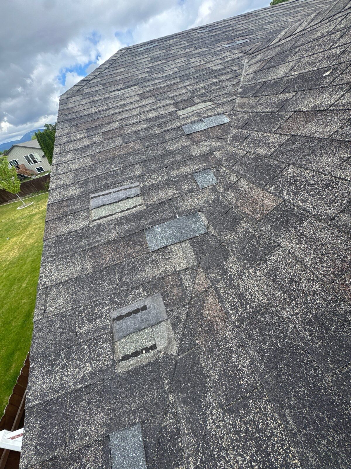 A worn North Idaho asphalt shingle roof with widespread granule loss and exposed fiberglass mat, past the point of more repairs