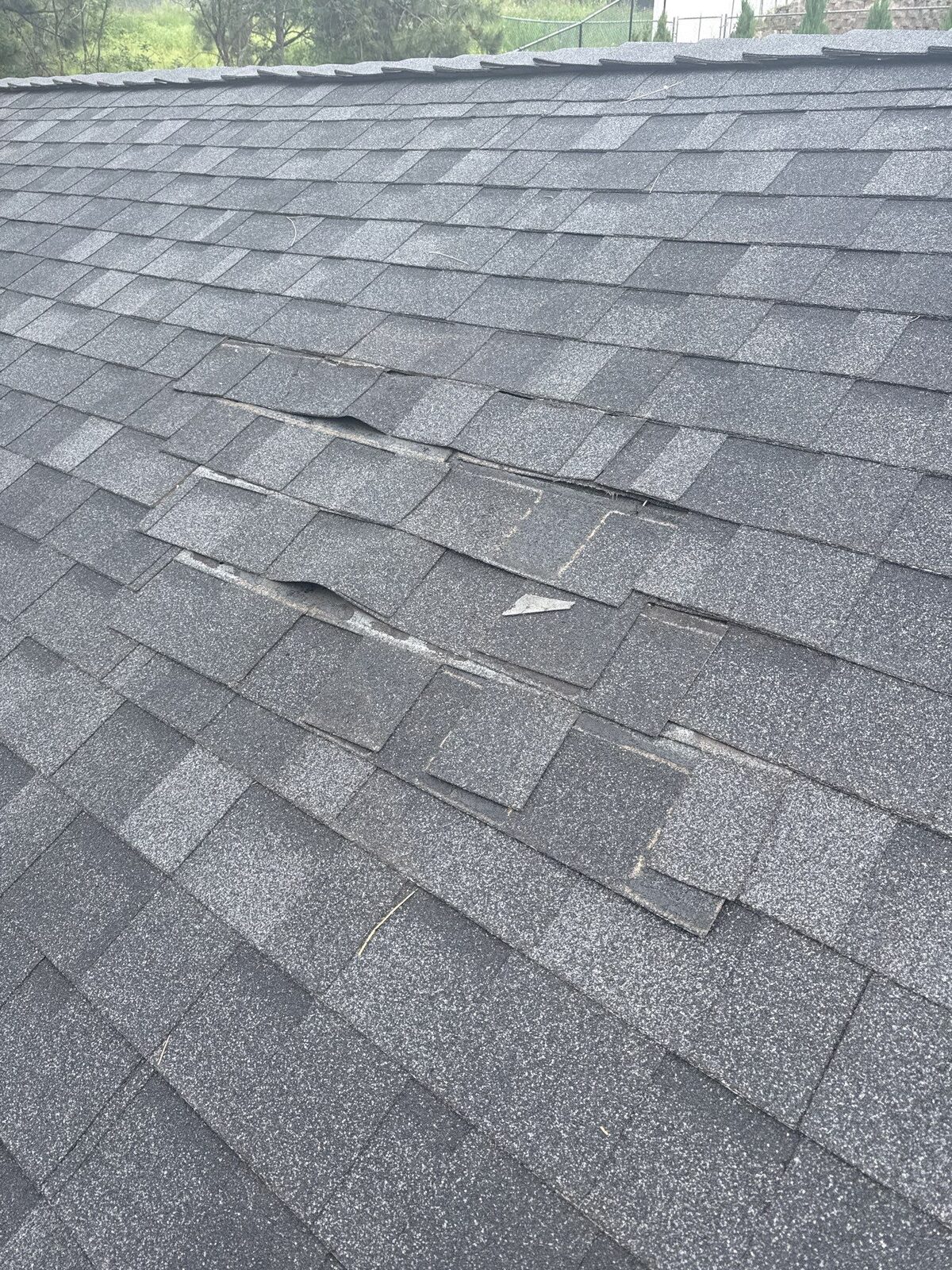 Wind-torn shingles on a newer North Idaho roof before repair, caused by a poor original install