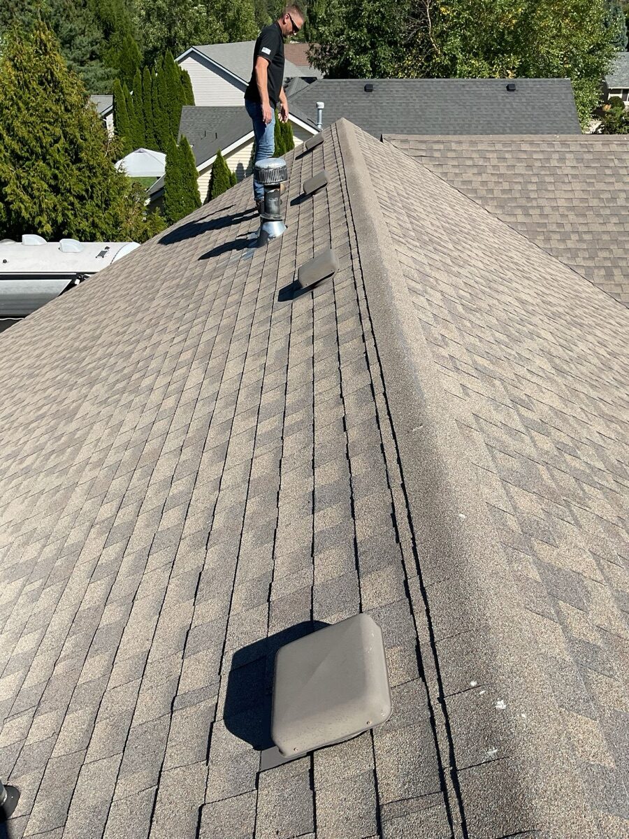 Aerial view of old roof showing worn shingles, vents, and inspector on ladder
