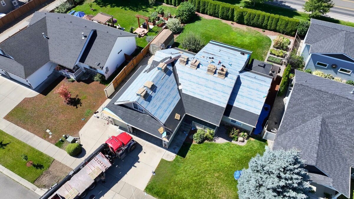 Aerial view of roof during tear-off — underlayment installed, dump trailer in driveway