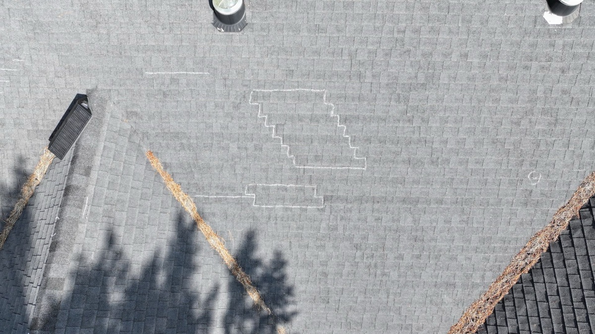 Top-down aerial showing chalk-outlined failed repair patch and pine needle debris in valleys