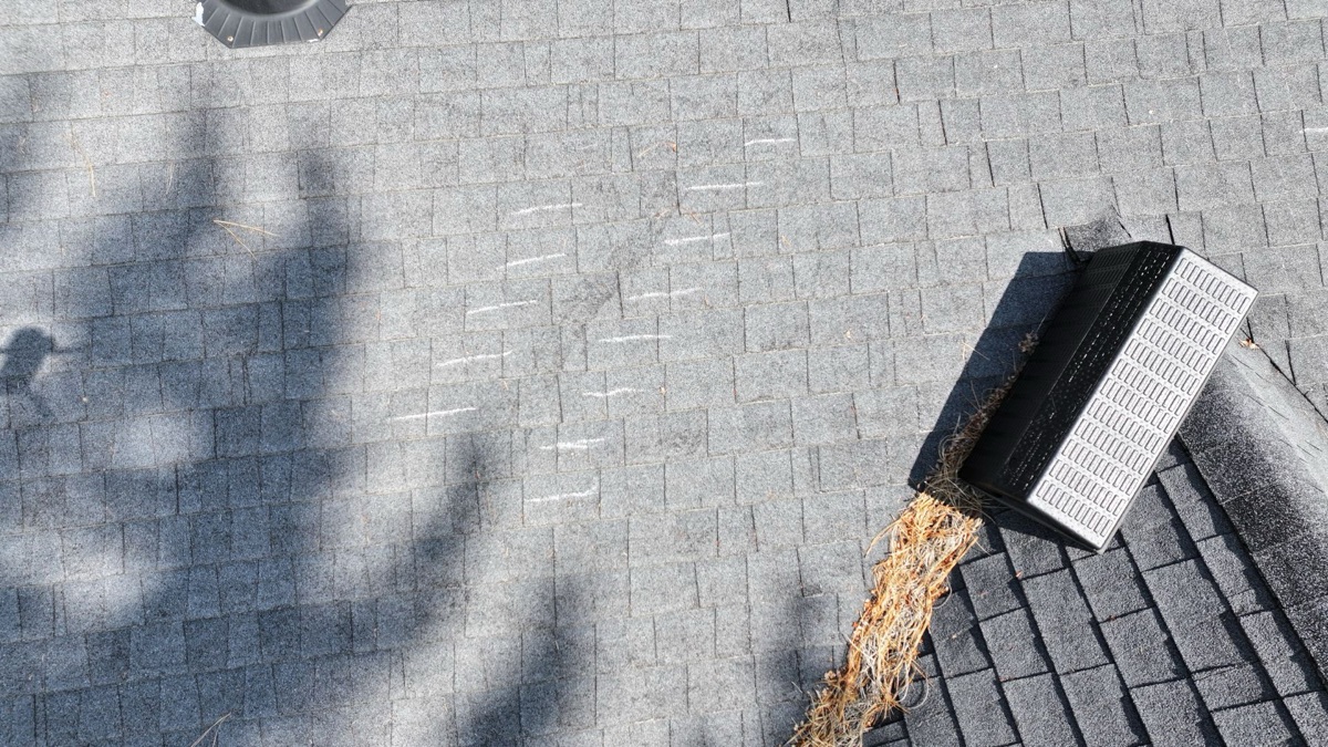 Close-up of worn shingles near roof vent with chalk inspection marks and valley debris